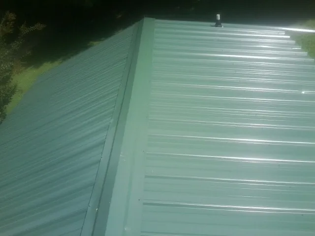 New green metal panels meeting at the ridge of a roof — Flat Roof Repair work by our crew in Princeton