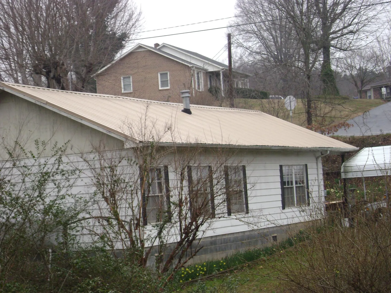 Tan metal roof on a white sided house set into a hillside — Commercial Roofing by Roofing Brothers in Princeton